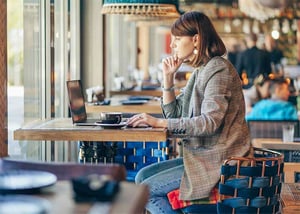 nainen istuu kahvilassa tietokoneen aarella